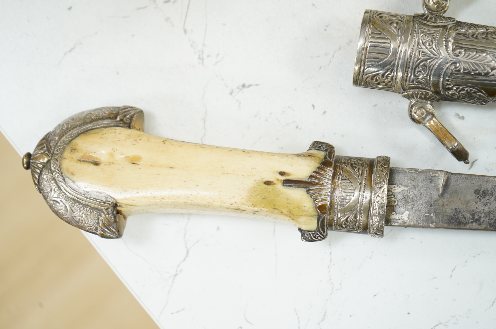A silver mounted Moroccan dagger jambya, with silver sheath and hilt, mounts chased with foliate and floral designs, and one piece bone grip, blade as found, overall length 42cm
